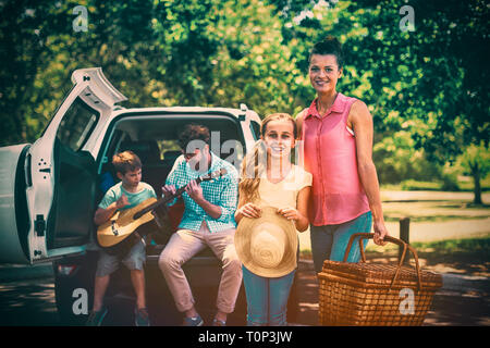 Ritratto di Madre e figlia in piedi con Cesto picnic mentre il padre e il figlio a suonare la chitarra in b Foto Stock