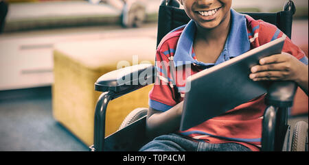 Scolaro disabili su sedia a rotelle con tavoletta digitale in libreria Foto Stock