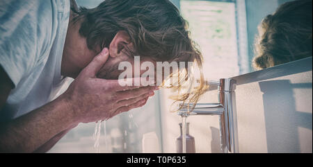 L'uomo lavare il viso con acqua in bagno Foto Stock