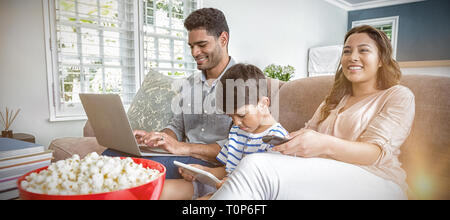 Madre di guardare la televisione mentre il padre e il figlio utilizzando laptop e tablet digitale Foto Stock