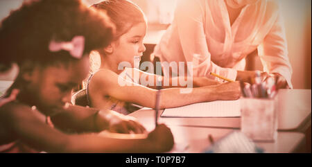 Docente aiutare i bambini con i loro compiti in classe Foto Stock