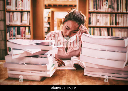 Teso giovane donna studiare in biblioteca Foto Stock