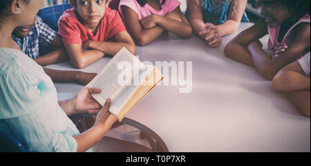 Insegnante libro lettura presso i bambini guardano a lei Foto Stock