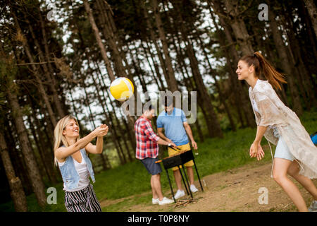 Giovani donne giocando a pallavolo su picnik in primavera la natura mentre gli uomini preparare grill Foto Stock