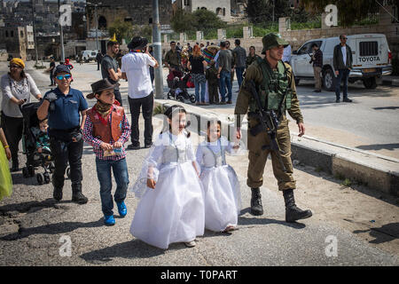 Hebron, Territori palestinesi. Xxi Mar, 2019. Un soldato israeliano tiene per mano con i bambini vestiti in costumi durante una parata celebra la festa ebraica di Purim. La carnevalesca Purim holiday è celebrata con sfilate in costume e parti per commemorare la liberazione del popolo ebraico dalla ad uno sterminio in persiano antico, come descritto nel libro di Ester. Credito: Ilia Yefimovich/dpa/Alamy Live News Foto Stock