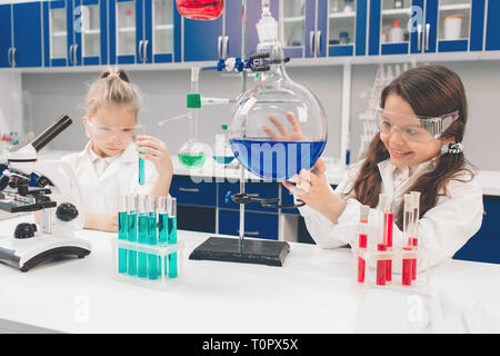 Due bambini piccoli in camice da laboratorio di chimica di apprendimento in laboratorio scolastico. Studiando gli ingredienti per gli esperimenti . Per i giovani scienziati occhiali protettivi mak Foto Stock