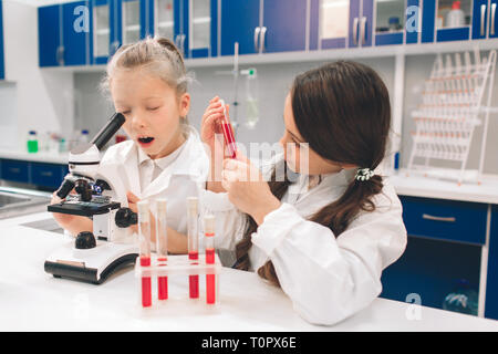 Due bambini piccoli in camice da laboratorio di chimica di apprendimento in laboratorio scolastico. Studiando gli ingredienti per gli esperimenti . Per i giovani scienziati occhiali protettivi mak Foto Stock