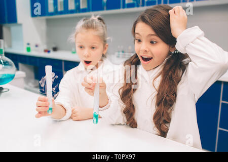 Due bambini piccoli in camice da laboratorio di chimica di apprendimento in laboratorio scolastico. Studiando gli ingredienti per gli esperimenti . Per i giovani scienziati occhiali protettivi mak Foto Stock