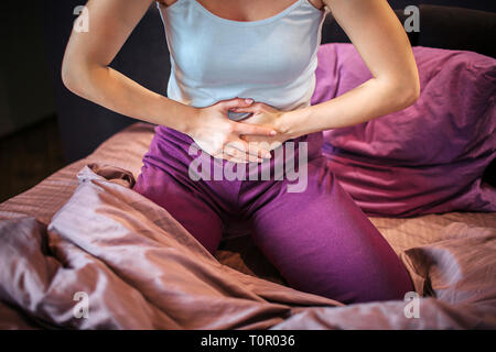 Vista di taglio del giovane donna soffre di dolore. Essa contiene entrambe le mani sul ventre. La donna si sente dolore ci. Lei è concentrata su questo problema. La donna si siede sul Foto Stock