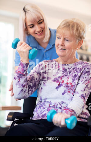 Fisioterapista femminile aiutando Senior donna in sedia a rotelle per sollevare pesi a mano Foto Stock