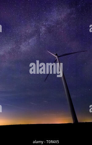 Una turbina eolica con bellissima via lattea in background con stelle luminose su terreno pianeggiante a mezzanotte Foto Stock