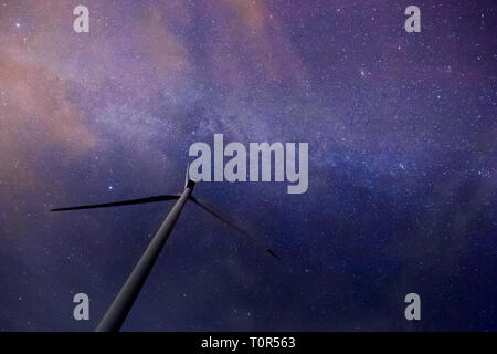 Una turbina eolica con bellissima via lattea in background con stelle luminose su terreno pianeggiante a mezzanotte Foto Stock