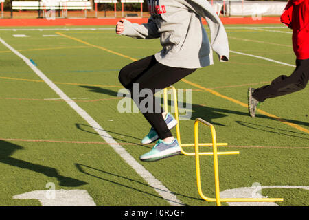 Un atleta in pista e la pratica sul campo salta gli ostacoli giallo su un tappeto erboso verde campo Foto Stock