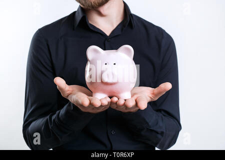 Imprenditore in camicia nera tenendo un salvadanaio. Risparmio di denaro Foto Stock