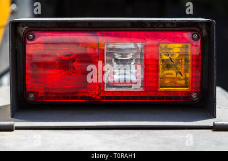 Faro rosso con ulteriori bianco e giallo, lampade colorate con bitume, su un corpo polveroso di macchine stradali, close-up su un sfocato sfondo scuro Foto Stock