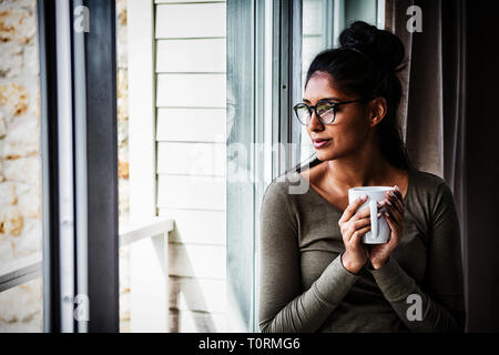 Donna con la tazza di caffè dalla finestra Foto Stock