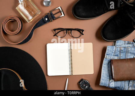 Mock up area di lavoro con hat, orologio, penna, profumo, jeans, portamonete, cinghia, calzature, notepad e occhiali su sfondo marrone. Concetto del papà. L piatto Foto Stock