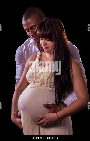 Un uomo e una donna incinta abbracciato guardando la donna di ventre Foto Stock