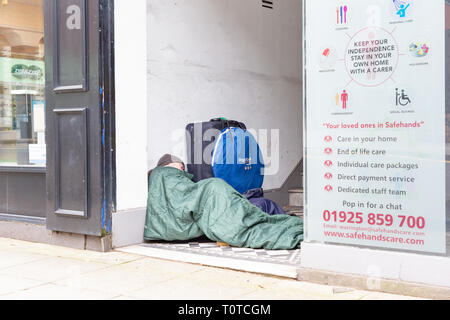 Senzatetto uomo dorme in modo irregolare a un negozio che porta in centro citta' di Warrington, Cheshire, Regno Unito Foto Stock