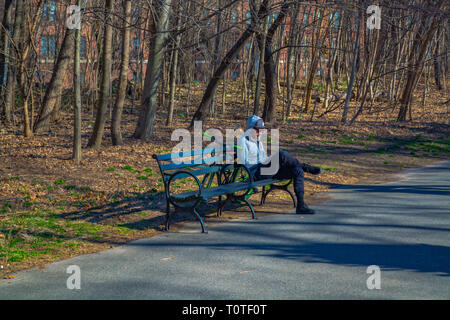 L uomo è seduta sul banco di lavoro e del controllo del suo smartphone nel Prospect Park durante la primavera, 2019 Foto Stock
