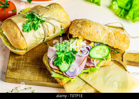 La porchetta italiana sandwich. La ciabatta in sandwich con prosciutto e pomodoro, formaggio, pepe, cipolla e insalata sul tagliere di legno con ingredienti. Foto Stock