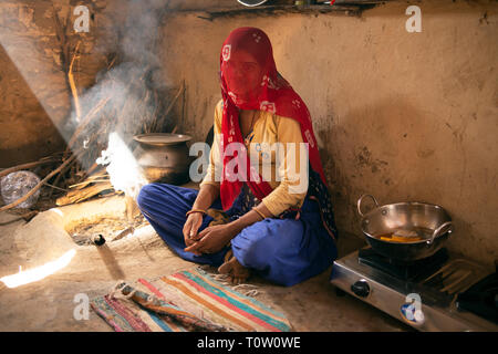 Una donna musulmana velata siede nella sua casa dal fuoco. Villaggio Kakani, Jodhpur, Rajasthan, India. Foto Stock