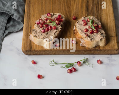 Due fette biscottate di anatra con prugne rillettes pate sul pane bianco con i semi di melograno su un pannello di legno su sfondo marmo. Spazio di copia Foto Stock