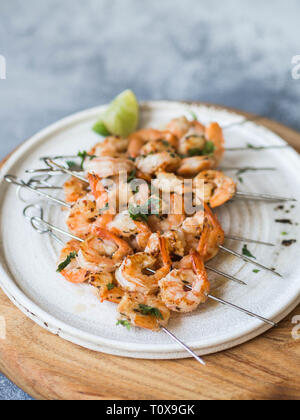 Grigliata di gamberi piccante su spiedini di metallo con il prezzemolo e il succo di lime sulla piastra bianca Foto Stock