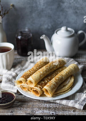 Russo in casa il lievito Pancake arrotolato in un tubo sulla piastra bianca, marmellata e tè nella tazza sul tavolo. Tradizionale frittelle di frumento per Shrovetide. Foto Stock