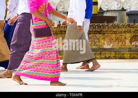 (Fuoco selettivo) Alcuni buddista birmano fedeli si cammina a piedi nudi intorno alla Shwedagon pagoda indossando un tradizionale e il longyi colorati. Foto Stock