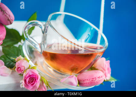 Rosa tea con macaron cookie e fiori di colore rosa su oscilla in movimento. Molla il concetto di energia su un vivace sfondo blu Foto Stock