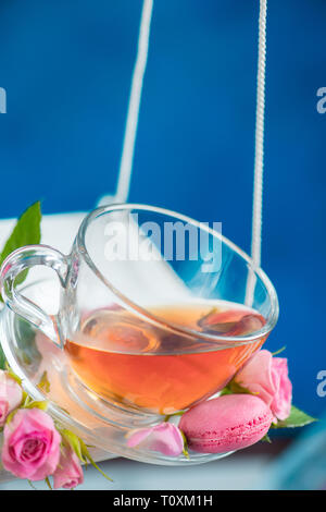 Altalene in movimento con la rosa tea, macaron cookie e fiori di colore rosa sulla molla concetto energetico su un vivace sfondo blu Foto Stock