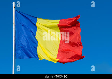 Bandiera della Romania sul post che si muovono nel vento. Il rumeno rosso e verde e la Bandiera blu sventola nel vento con chiaro sfondo blu. Foto Stock