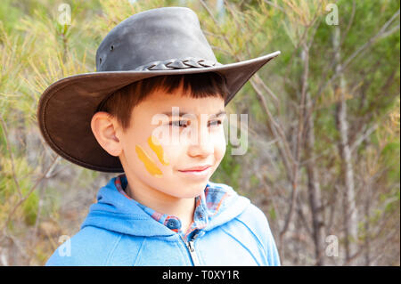 Giovane ragazzo in cappello da cowboy nel bush australiano, con ocra gialla della vernice sul suo volto Foto Stock