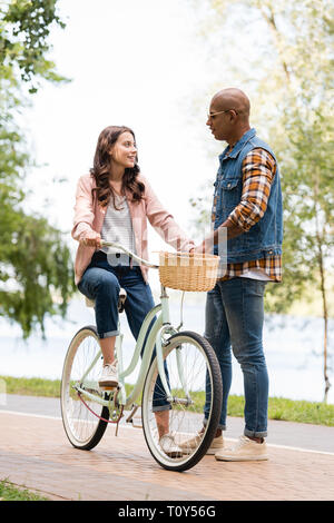 Felice americano africano un uomo guarda allegro ragazza Bicicletta Equitazione Foto Stock