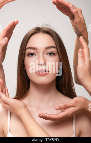 Ritratto di giovane e bella donna circondata da mani femminili isolato su grigio Foto Stock