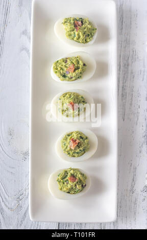 Guacamole e pancetta deviled le uova sulla piastra bianca Foto Stock