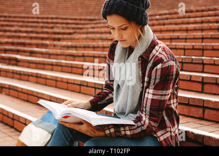 Giovane donna leggendo un libro sul university scale. Femmina caucasica studente la preparazione per gli esami presso il college. Foto Stock