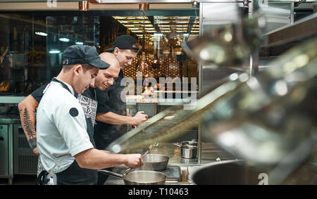 Scuola di cucina. Strict giovane chef di grembiule guardando attentamente come suo assistente cucina presso il ristorante la cucina. La preparazione di alimenti Foto Stock