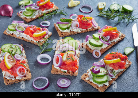 Vista aerea del pane croccante detto "Knäckebrot" aperto di fronte a sandwich con salmone affumicato, morbida crema di formaggio, il cetriolo, la cipolla rossa, cosparsi di semi di lino in un calcestruzzo ta Foto Stock