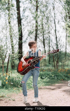 Bambina a suonare la chitarra in piedi sul percorso nel parco della città Foto Stock