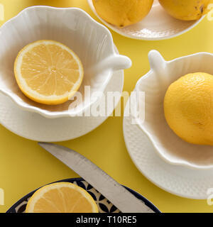 Crudo fresco di limoni e porcellane tablewares fresco su sfondo giallo. Still Life, sfondo, fresh food design Foto Stock
