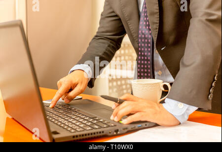 Imprenditore mano premere il tasto Invio della tastiera del notebook con tazza di caffè sul tavolo. Foto Stock