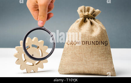 Sacco di denaro con la parola crowdfunding e ingranaggio. Il concetto di raccolta di fondi per una società crowdfunding o un avvio. La sponsorizzazione di un progetto. Sviluppo Foto Stock
