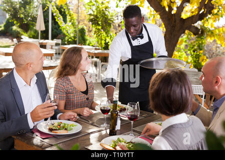 Cameriere che serve pasti al cordiale compagnia presso il ristorante all'aperto Foto Stock