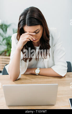 Sconvolto imprenditrice seduta a tavola con il computer portatile in ufficio Foto Stock