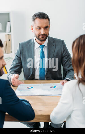 Messa a fuoco selettiva di advisor nella tuta discutendo i documenti con gli investitori in ufficio Foto Stock