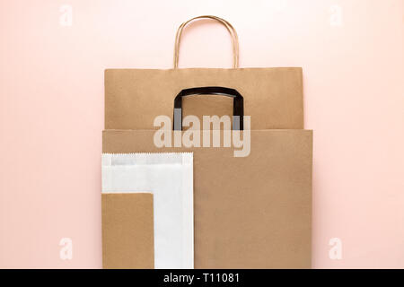 Marrone e bianco vuoto di carta kraft sacchi su sfondo rosa. Vista dall'alto. Eco di confezionamento o di imballaggio del concetto dei pasti Foto Stock