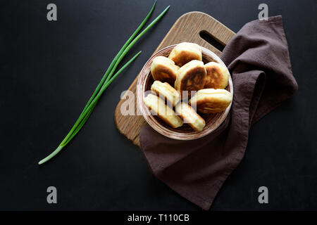 Polpette fritte o torte riempito di cipolla verde e uova sul legno scuro dello sfondo. Pirozhki tradizione russa cibo. Foto Stock