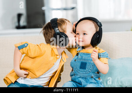 Adorabili preschooler boy in cuffie fratello baciare sulla guancia a casa Foto Stock